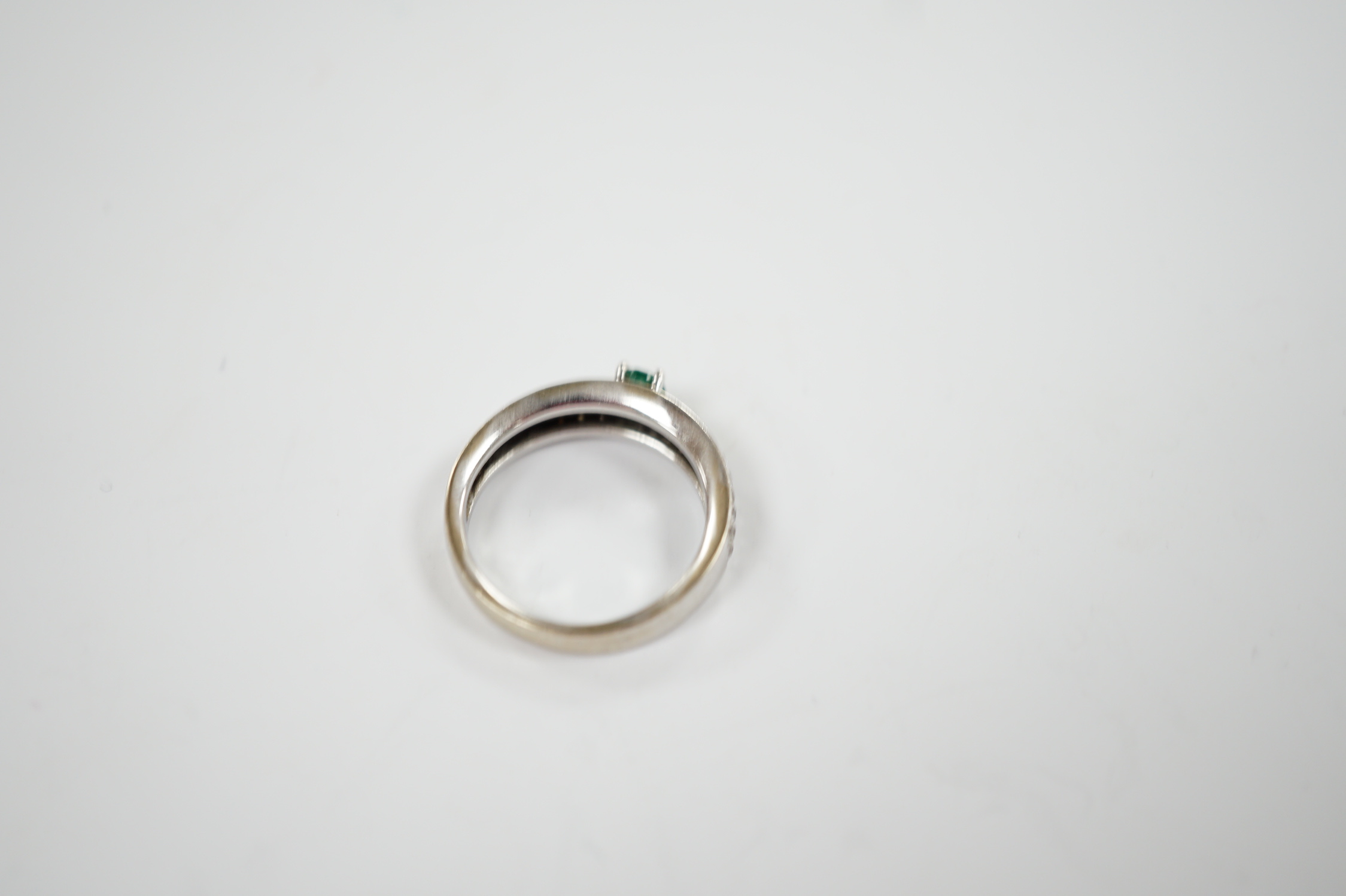 A modern 18ct white gold and single stone oval cut emerald set ring, with pave set diamond shoulders, size L/M, gross weight 4.3 grams.